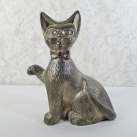 Vintage Siamese cat metal bank with original metal stopper. Wearing a bow tie, one paw is raised in a wavelike pose: Front View - Click to enlarge